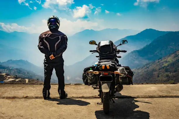 man motorcyclist standing at hill top with his loaded motorcycle and pristine natural view image is taken at bomdila arunachal pradesh india.