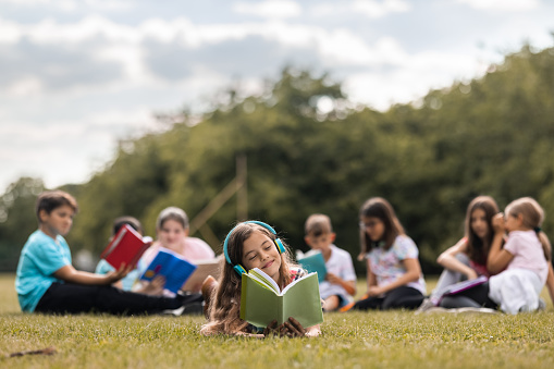 Happy schoolgirl reading a book whit her friends on the meadow