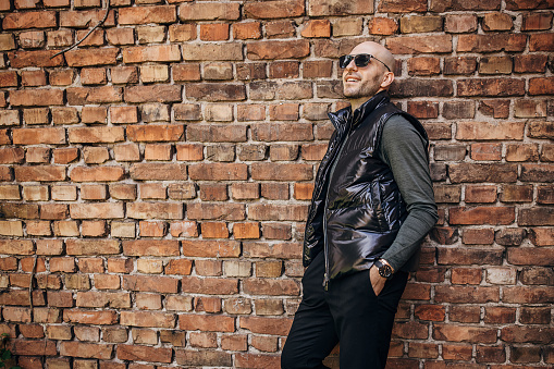 One man, fashionable male standing alone by a brick wall.