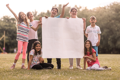 Large group of happy children shouting and looking at camera while holding blank paper in the nature