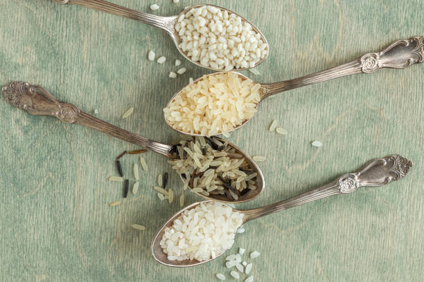 close up different types of rice in spoons with copy space. Wild rice, sushi rice, shredded and steamed rice on a green wooden background. healthy food concept. Soft focus stock photo
