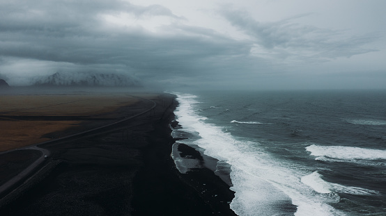 Dramatic drone panoramic photo of the black sand Diamond beach, stormy ocean, mountains and glacier during moody summer day at South Iceland