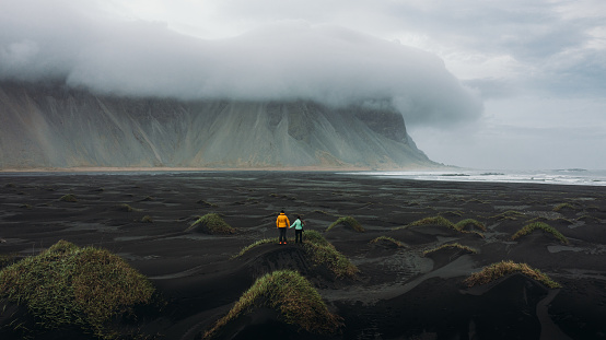 Drone photo of a young couple of traveler enjoying the cloudy morning walking at the black sand remote Stokksnes beach with mounain view at East Iceland
