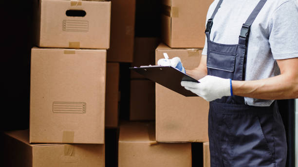 istock A young handsome smiling worker wearing uniform is standing next to the van full of boxes holding a clipboard in his hands. House move, mover service 1322696342