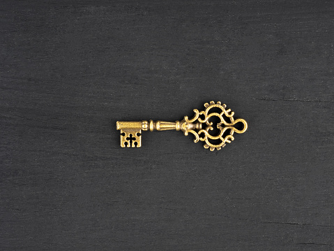 Bronze color antique key on black wooden background with copy space