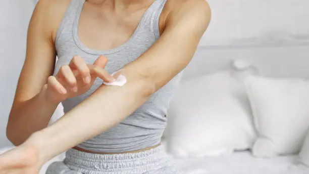 Girl in a studio. Lady with cream. Woman in a gray t-shirt. Girl sitting on a bed.