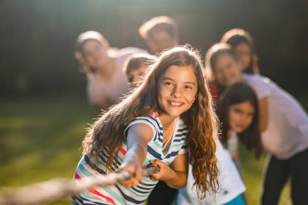 Group of kids in a tug-of-war game outdoors Group of children pulling a rope in public park summer camp stock pictures, royalty-free photos & images