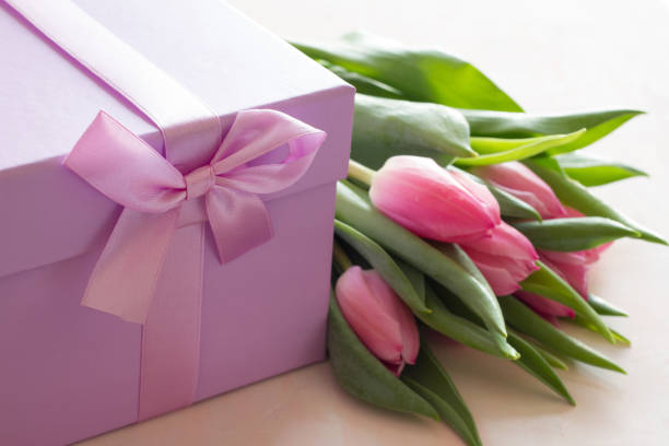 istock Decorative gift box with purple ribbon and tulips on light background 1322697655