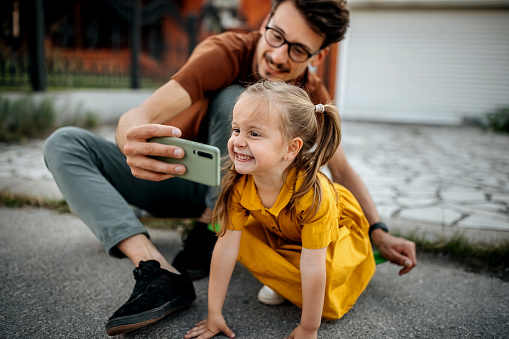 Father and daughter sit on a skateboard and take selfies