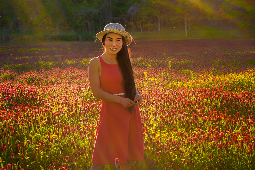 Full body portrait of Chinese woman in red dress and straw hat in field of colorful wildflowers at sunset
