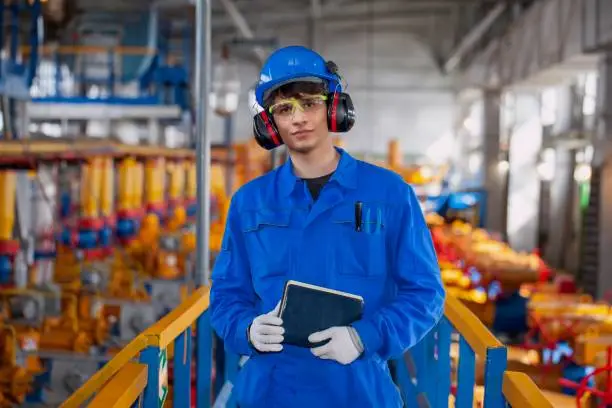 The mechanic - the repairman tightens bolts on a flanged connection of pipeline armature, operator production gas, worker in personal protective equipment close-up portrait, safety precautions