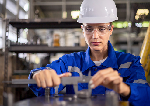 Quality control female engineers measure the production of mechanical material part.