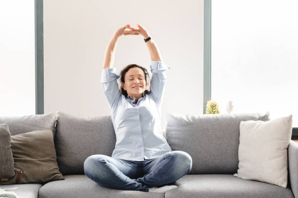 Middle-aged mature caucasian woman sitting on the couch sofa in living room, relaxing and having rest , stretching in yoga position after working day. Female freelancer having break after remote job mujer caucásica madura de mediana edad sentada en el sofá del sofá en la sala de estar, relajándose y descansando, estirándose en posición de yoga después del día de trabajo. mujer freelancer teniendo descanso después de un trabajo remoto
