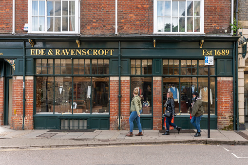 Exterior of Ede & Ravenscroft shop in Cambridge, a city in England famous for its prestigious university, established in the 12th century. There are young students walking past the shop.