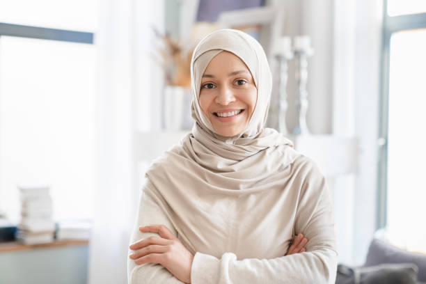 mujer musulmana madura de oriente medio con hiyab, madre, tutora, esposa de pie con los brazos cruzados en casa. retrato frontal de una mujer árabe - nikab veil islam arabia fotografías e imágenes de stock