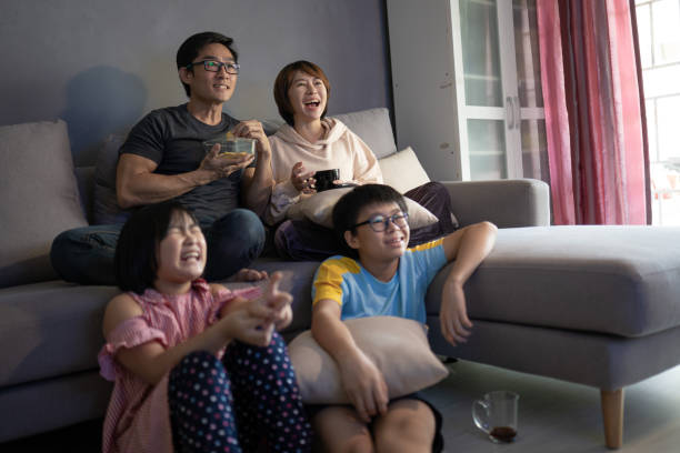 asian chinese family sitting on sofa watching television at home together. - ding imagens e fotografias de stock