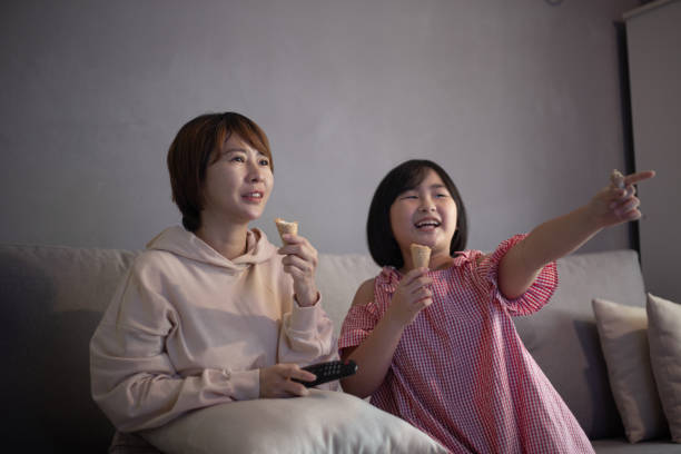 Asian Chinese mother and daughter sitting on sofa watching television at home together. Asian Chinese mother and daughter sitting on sofa watching television at home together. asian kids watching tv stock pictures, royalty-free photos & images