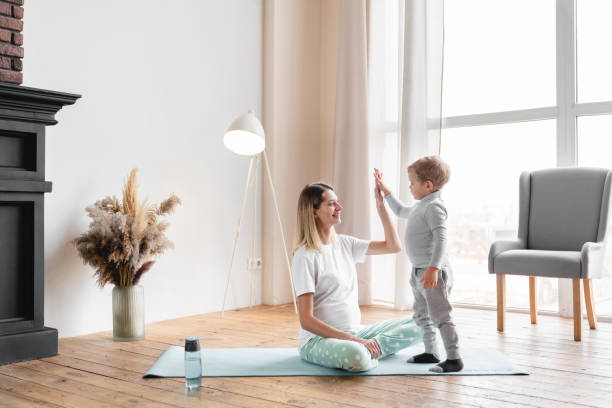 giovane madre incinta mamma che si allena sul tappetino fitness con il suo figlio piccolo, dando cinque alti. sport, alleno yoga con i bambini. futura madre, periodo prenatale, in attesa di un concetto di bambino - child exercising little boys toddler foto e immagini stock