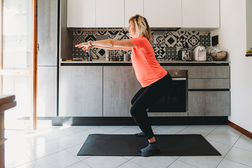 Pregnant woman exercising at home in the kitchen. She's in squatting position.