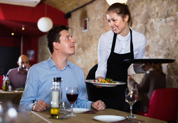 istock Polite waitress serving ordered dishes to smiling man at restaurant 1322718271