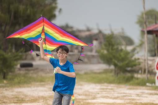 Asian Chinese teenager boy playing and flying kite at beach in weekend.