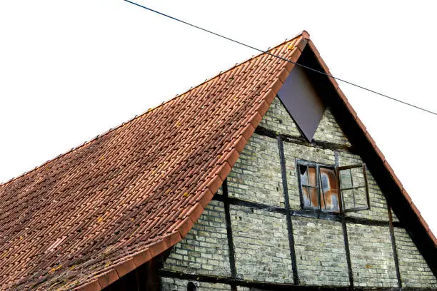 Old half-timbered barn. Weathered building with an old open window. Roof with red roof tiles