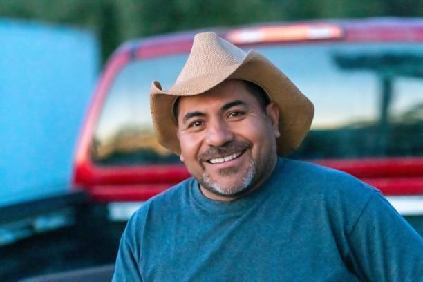 Smiling Hispanic farm worker posing wearing a cowboy hat looking at the camera