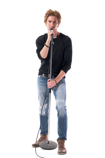 Cool young handsome male rock music singer singing on microphone looking at camera. Full body length isolated on white background.