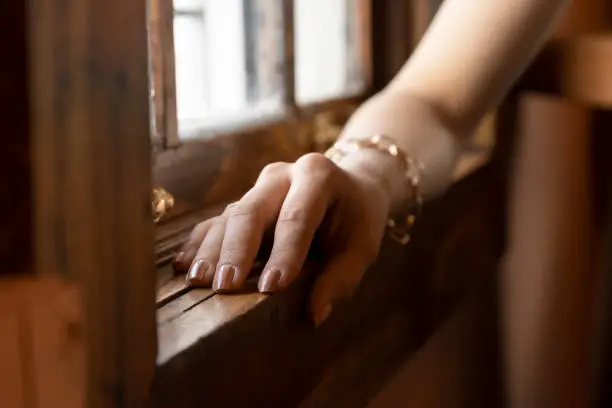 hand of a person with simple but elegant nails, wears a gold bracelet, the arm is close to a wooden vein, studio and parts of the body