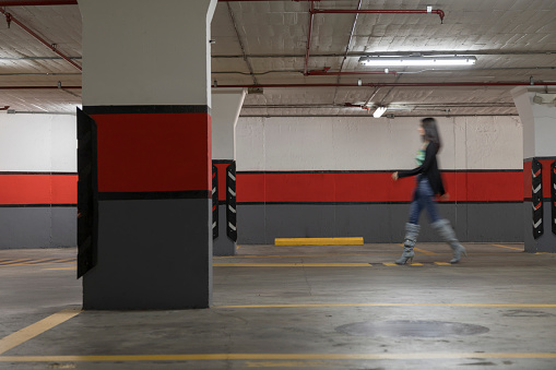 colorful underground parking without cars with artificial lighting, with tall, slim female pedestrian walking, wearing casual clothes, city lifestyle