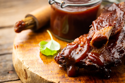 Delicious BBQ baby-back ribs with tangy sauce and a basting brush on wooden cutting board