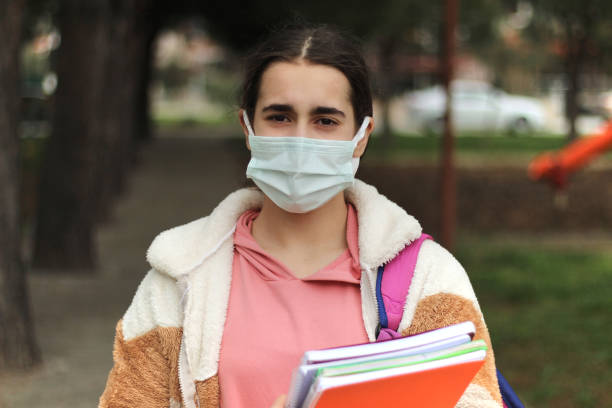 istock Schoolgirl in a protective mask with a backpack and a textbook in her hands. 1322732008