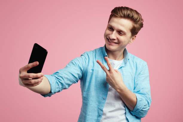 istock Man in trendy outfit smiling and showing peace gesture while taking selfie 1322735958