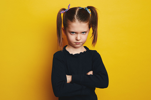 Offended Kid Concept. Portrait of sad girl crossing arms standing isolated over yellow studio background