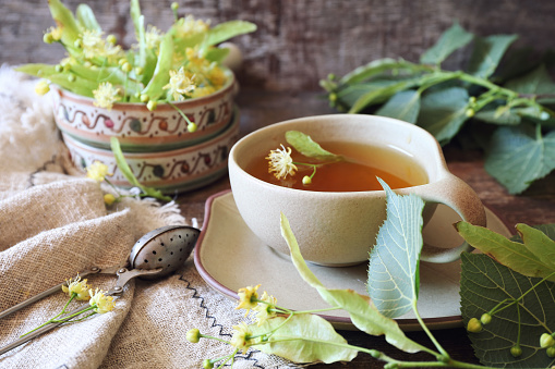 Cup of herbal tea with linden flowers on old wooden background