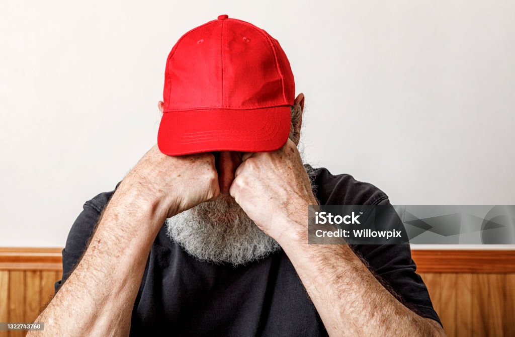 Red Hat Redneck Senior Man Crying A senior adult man redneck hillbilly Trump supporter wearing an iconic red baseball style hat is crying over spilt milk - in this case because he believes the ludicrous Trump Big Lie that the 2020 USA presidential election was implausibly and impossibly somehow "stolen" from the Republican political party, it's voters, and it's big mouth former guy loser. Not true - it wasn't. This pathetic man has been hoodwinked and scammed. US Republican Party Stock Photo