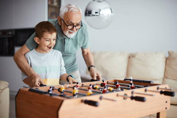 heureux garçon s’amusant pendant que son grand-père lui apprend à jouer au baby-foot à la maison. - grandson photos et images de collection