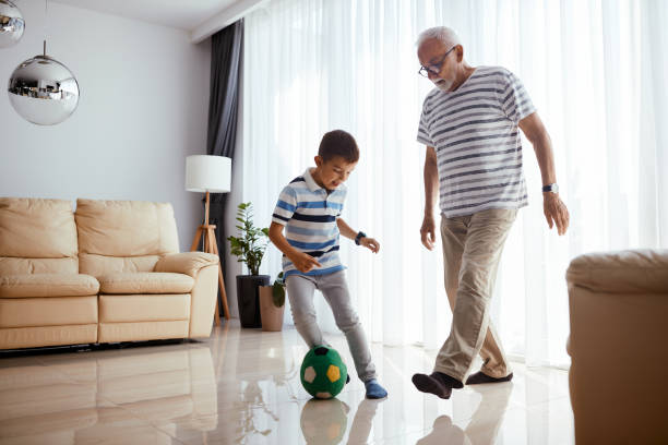 ragazzino giocoso che si diverte mentre gioca a calcio con il nonno a casa. - soccer child indoors little boys foto e immagini stock