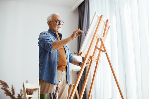 Senior man painting on canvas while enjoying creative time at home.