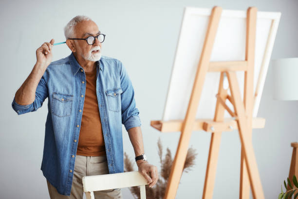 istock Senior man thinking while painting on canvas at his home workshop. 1322745175
