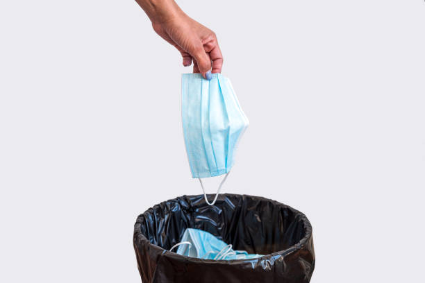 istock Woman throwing used protective surgical mask into the garbage bin 1322752177