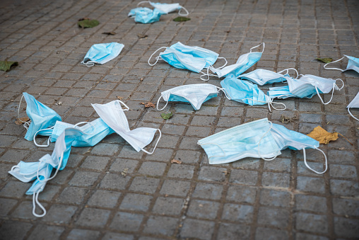 Remnants of used dirty hygienic discarded medical masks for protection Covid-19 (coronavirus), SARS-CoV-2 or other viruses drop down or leave on the floor of sidewalk in the city. Environmental pollution, ecology problems and medical equipment waste concept.