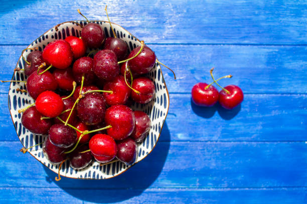 istock Ripe red cherries bowl with water drops on blue wooden table. Top view with copy space 1322757765