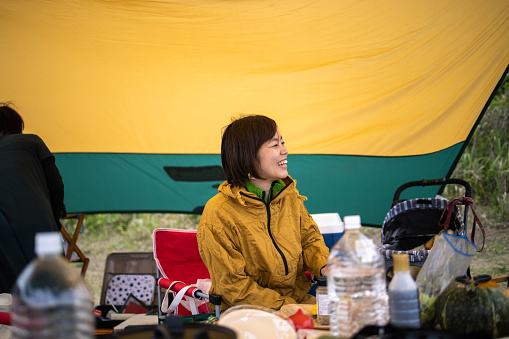 Japanese families camping together. Setting up tents on large green field and eating barbecue for lunch and dinner. Communicating with family and friends.