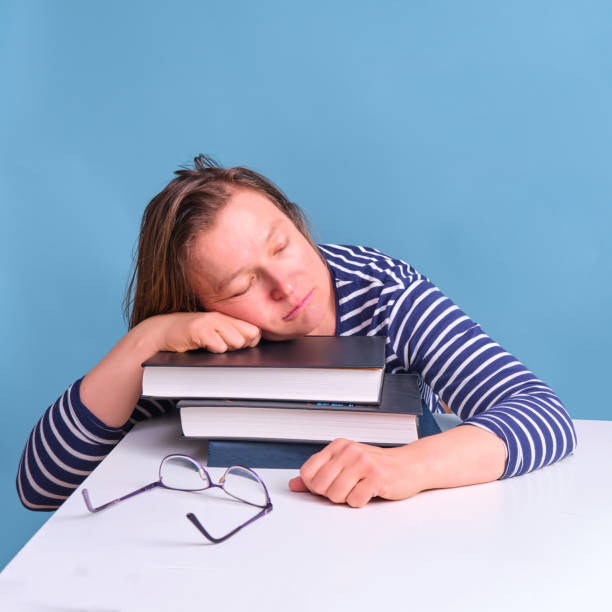 istock Adult tired woman sleeping on books while studying, blue background 1322770746