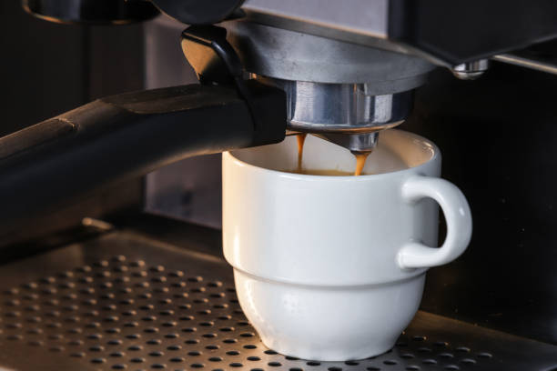 istock Close up, coffee from espresso machine, in small white ceramic cup, the essence or extract falling from the filter, appliance for a variety of caffeinated beverages, hot drink served. 1322774778