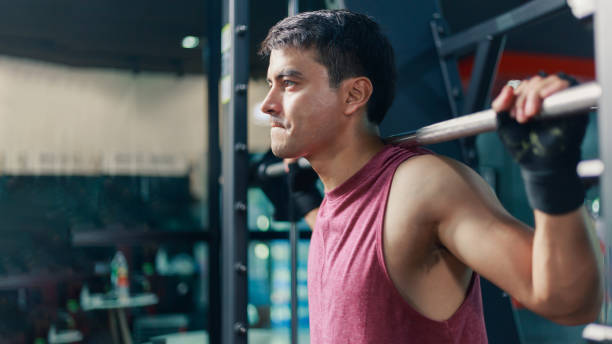 istock Young fit attractive Caucasian man in active wear working out using weight bar shoulder press machine at the sport club center. Concentration motivation exercise fitness. People lifestyle concept. 1322775895
