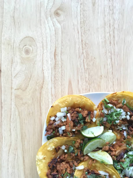 overhead shot of Mexican tacos al pastor, with marinated meat, onion, pineapple, cilantro, corn tortilla on a flat plate and wooden background, with copy space