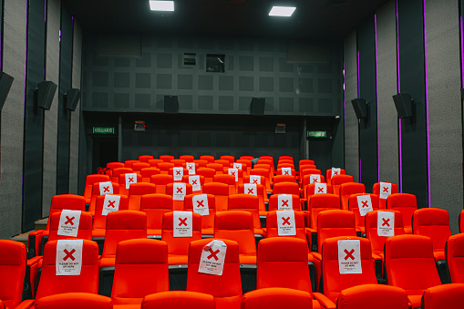 row of red cinema seats in empty movie theater auditorium with banner social distancing of COVID-19 new normal
