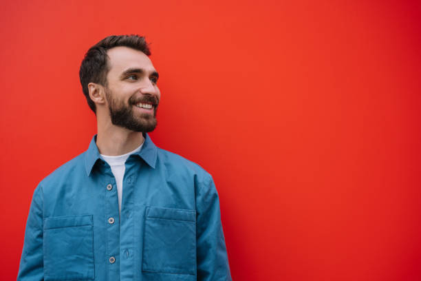 Smiling man wearing stylish casual shirt isolated on red background. Copy space, advertising concept Young smiling man wearing stylish casual shirt isolated on red background. Copy space, advertising concept looking away stock pictures, royalty-free photos & images